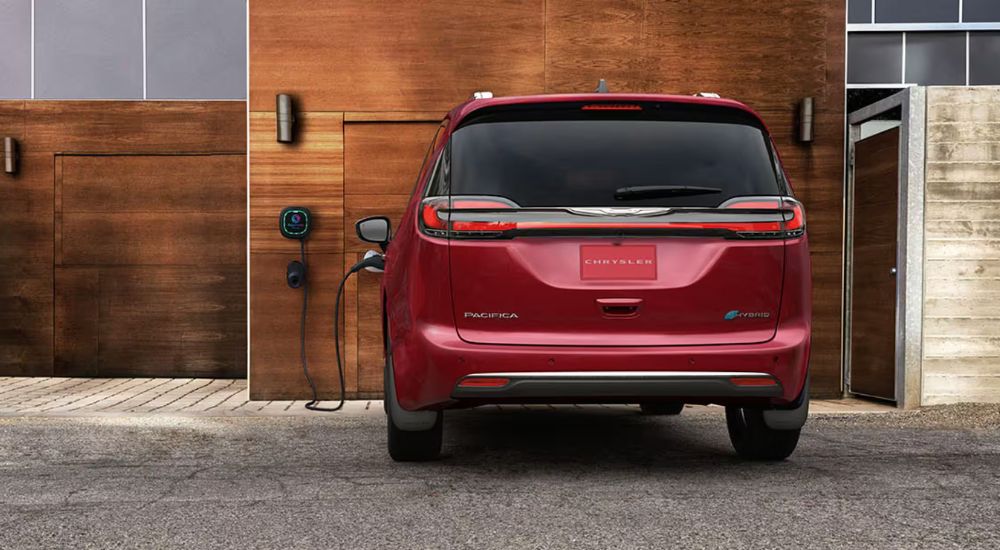 Rear view of a red 2025 Chrysler Pacifica PHEV charging outside a home.
