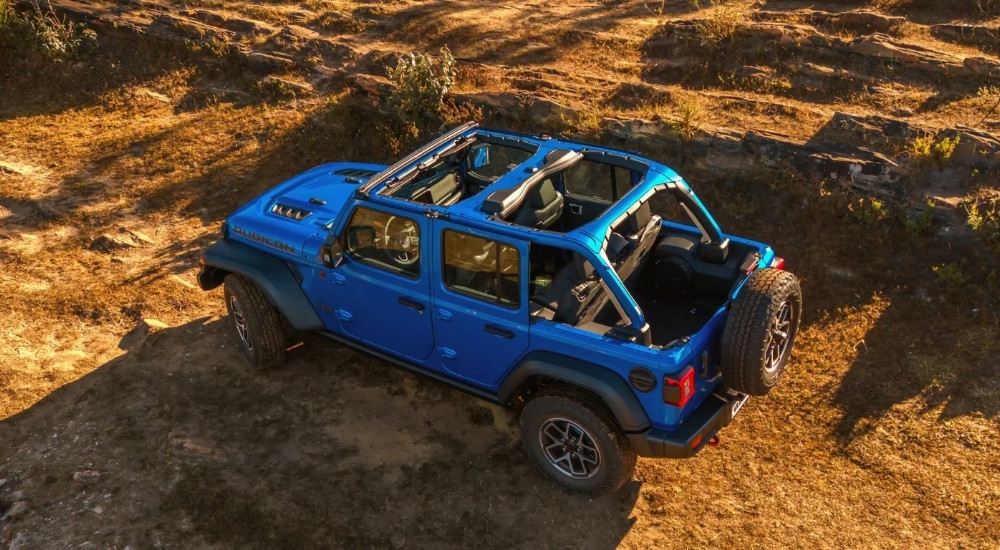 A blue 2024 Jeep Wrangler Unlimited Rubicon is driving on a trail.