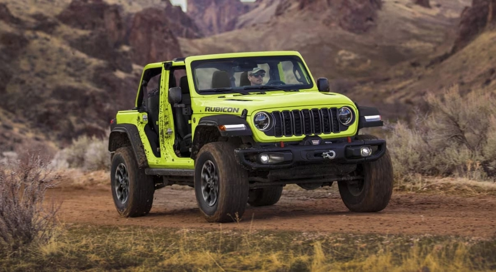 A green 2024 Jeep Wrangler Unlimited Rubicon is driving on a trail.