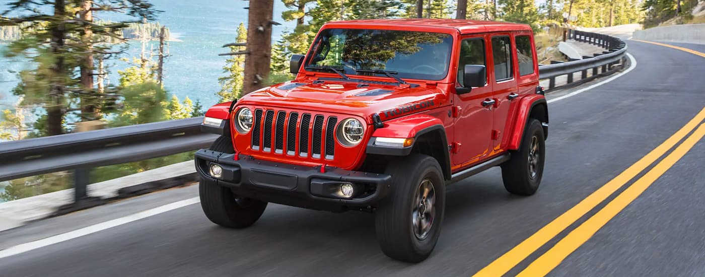 A red 2024 Jeep Wrangler Rubicon Unlimited driving down a road.