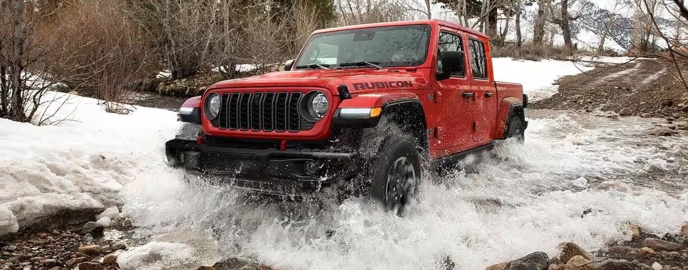 A red 2024 Jeep Gladiator Rubicon driving over a shallow river.