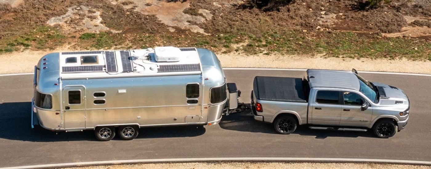 A silver 2025 Ram 1500 is shown towing a camper.