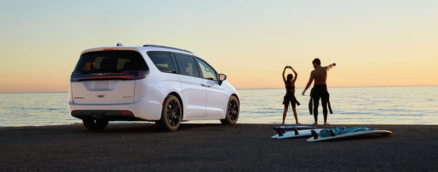 Rear view of a white 2025 Chrysler Pacifica Limited parked near water and people doing yoga.