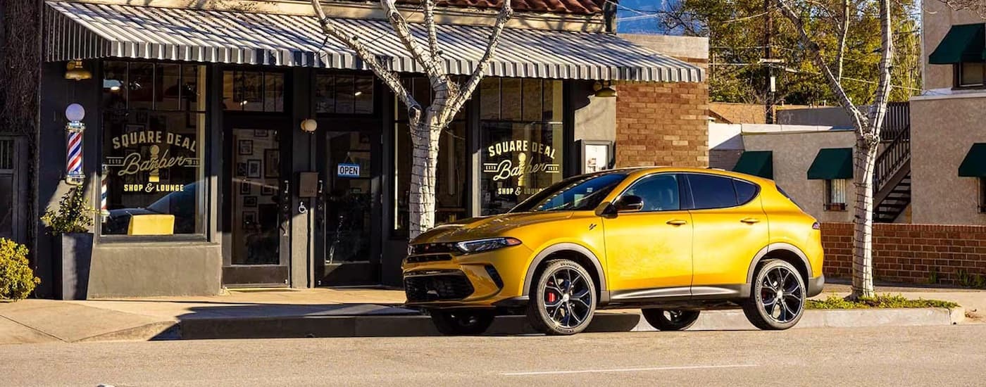 A yellow 2024 Dodge Hornet parked on the street in front of a barber shop.