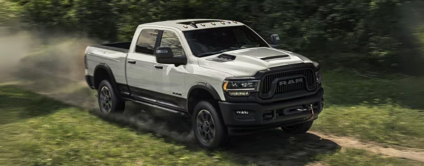 A white 2023 Ram 2500 is shown kicking up dust on a trail in the woods.